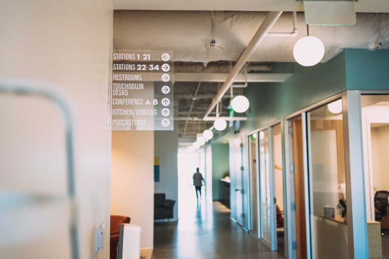 Modern coworking space hallway with directional signage and pendant lights.