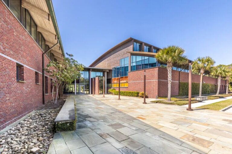 Modern brick building with a curved roof, courtyard, and palm trees.