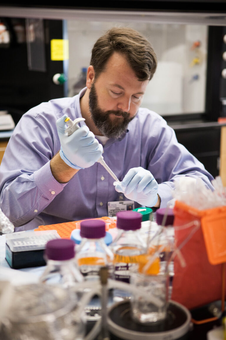 Scientist using a pipette to transfer liquid samples in a laboratory.