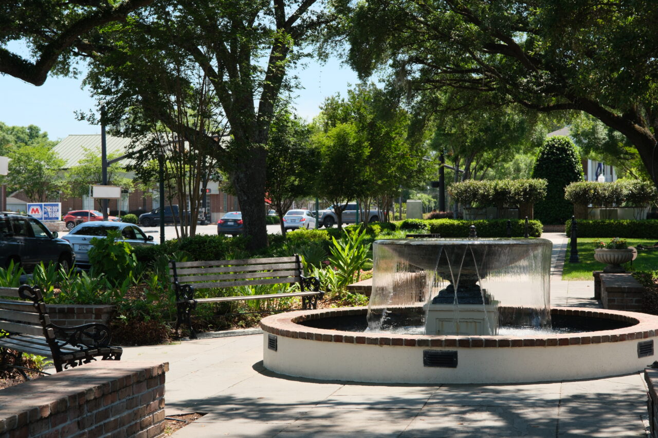 Fountain in a shaded park square in Charleston with benches and greenery.