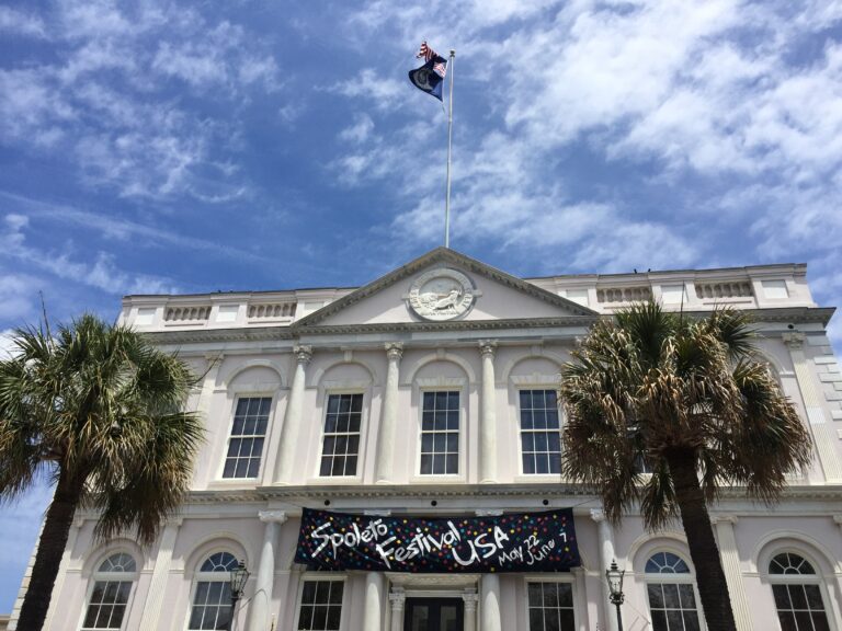 Historic white building displaying a Spoleto Festival banner under a blue sky.