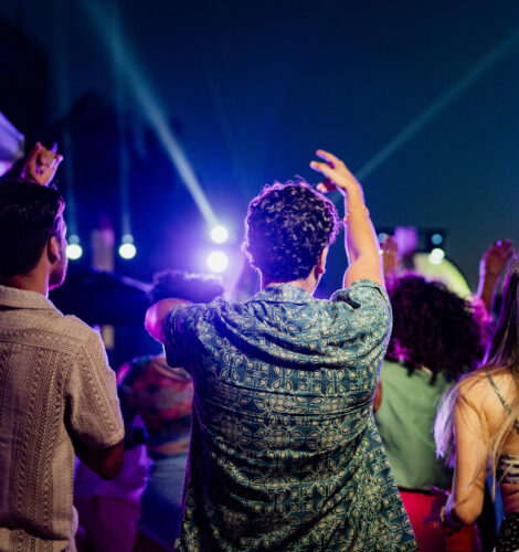 Three people dance in a crowd while at a festival at night.