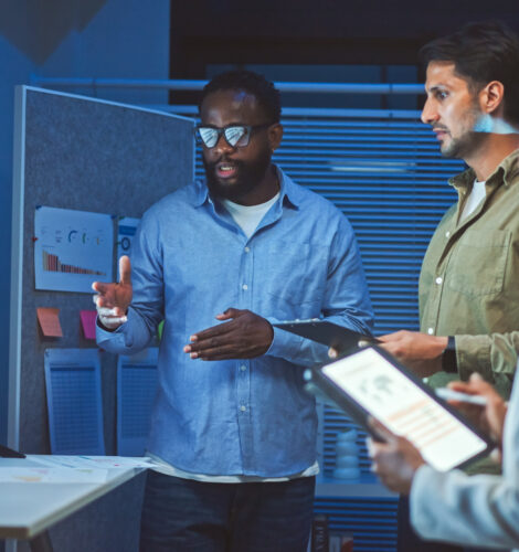 Three coworkers analyze graphs on a large monitor in an office.