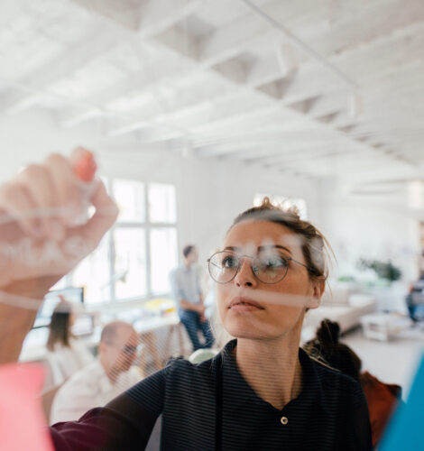 A woman writes on a clear board in an office.