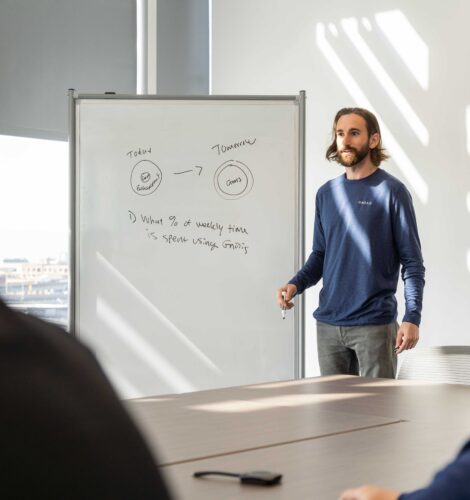 A man uses a whiteboard to give a presentation in a boardroom during the day.