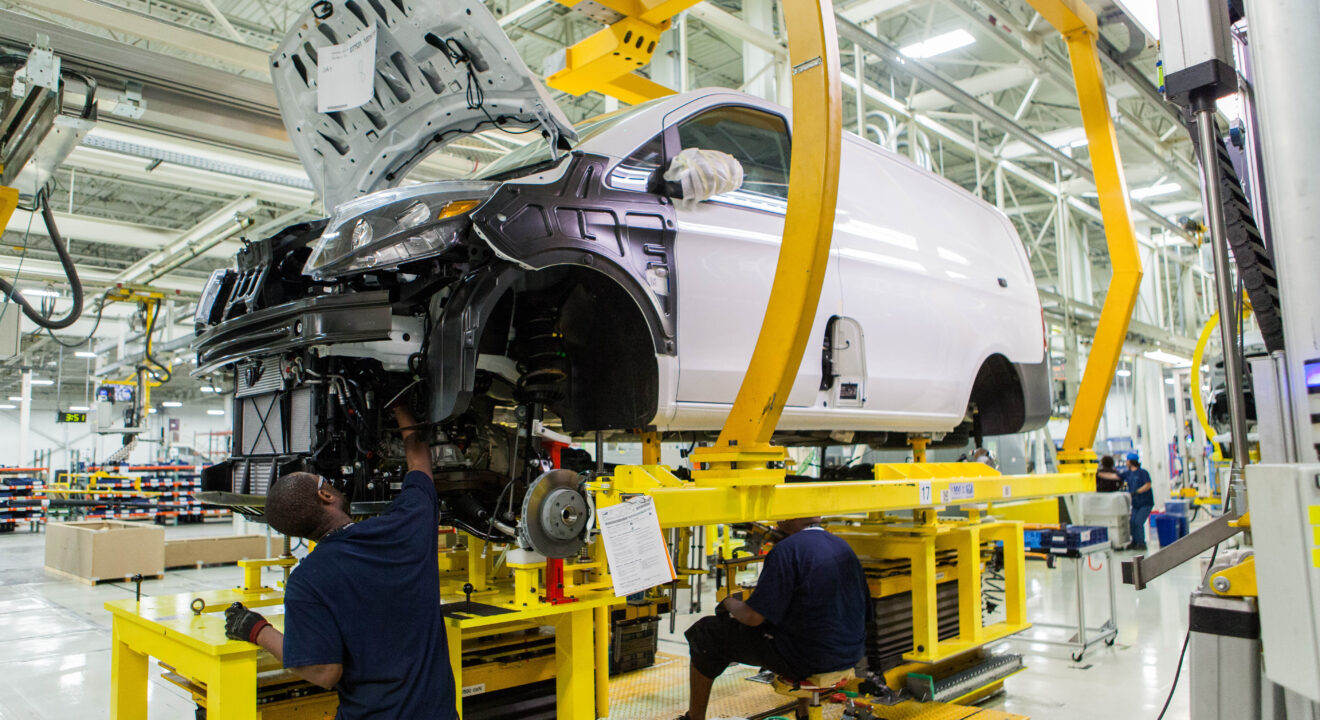 A manufacturing employee works on the body of a car in a factory.