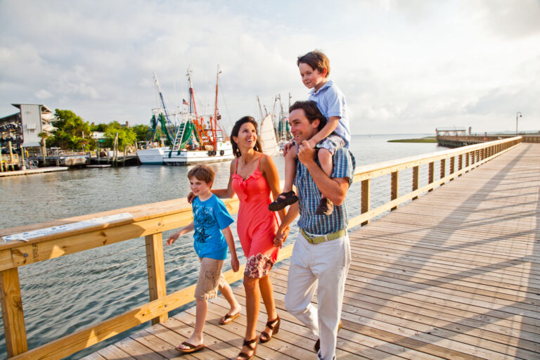 A family of four smiles as they walk down a boardwalk during the day.