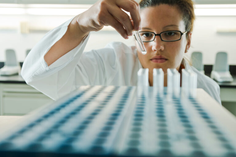 A scientist performs a quality assurance inspection on a series of test tubes.