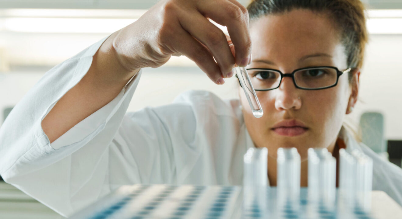 A scientist performs a quality assurance inspection on a series of test tubes.