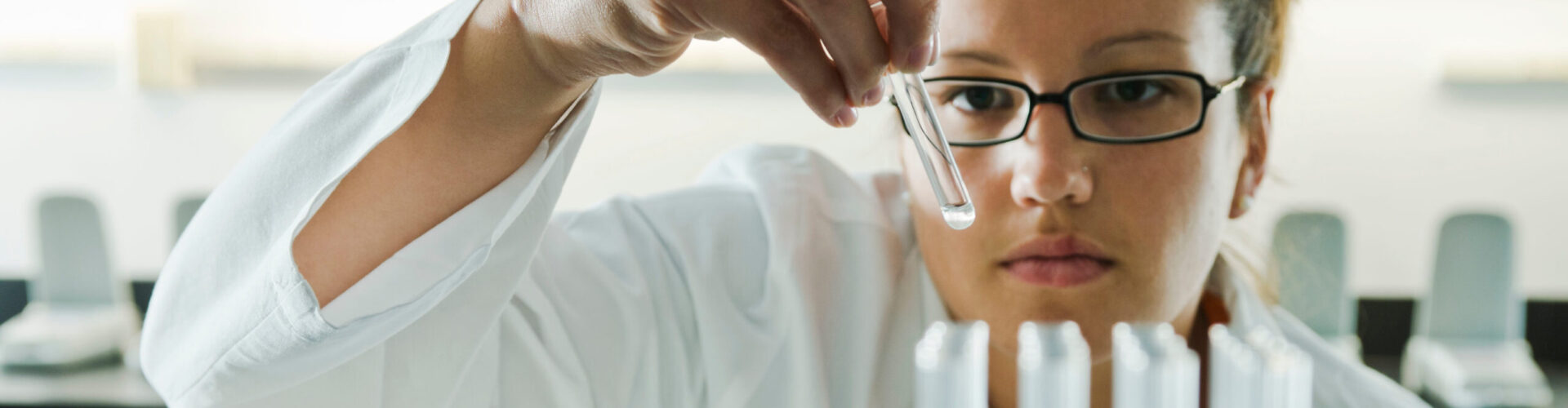 A scientist performs a quality assurance inspection on a series of test tubes.