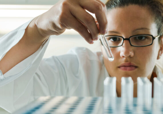 A scientist performs a quality assurance inspection on a series of test tubes.