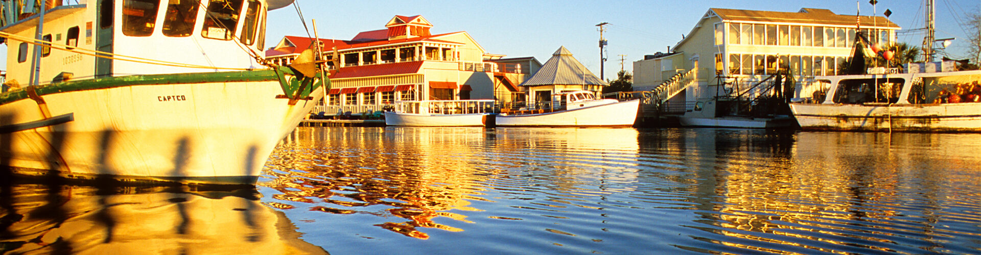 Boats at dock by a boardwalk at sunset.