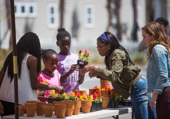 A group of women and children look at flowers at a farmer's market.