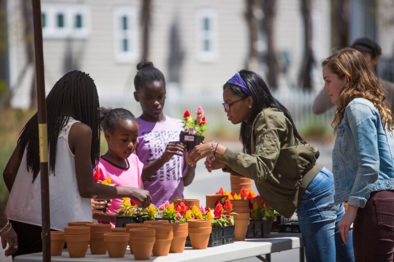 A group of women and children look at flowers at a farmer's market.