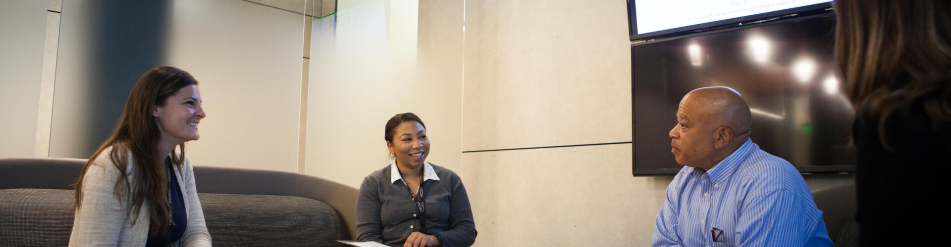 Three business people sit around a casual office table and talk together.