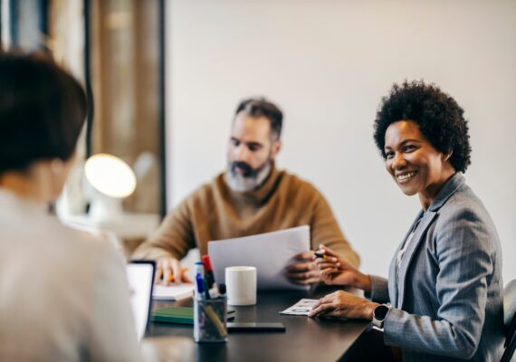 A business woman smiles at her coworker while at a table together.