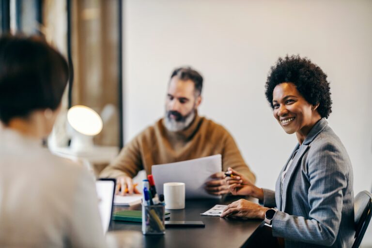 A business woman smiles at her coworker while at a table together.