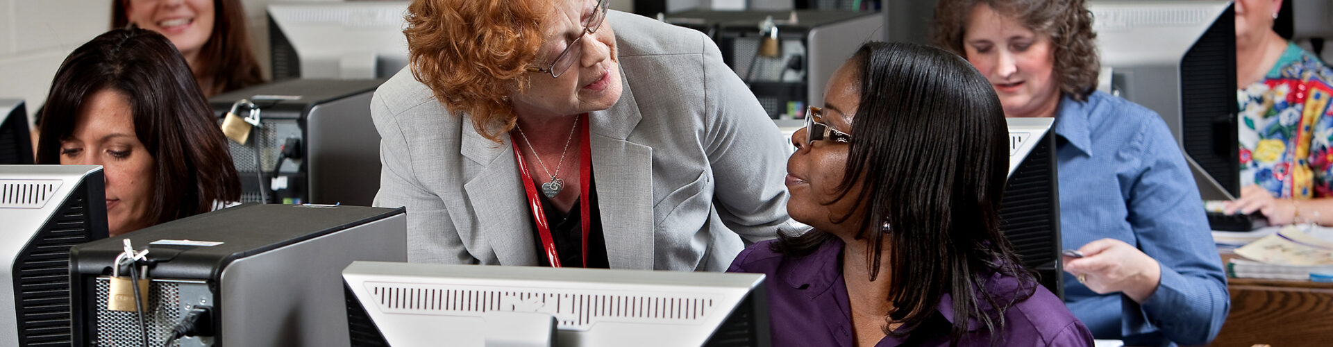A woman at a desktop computer receives guidance from a supervisor.