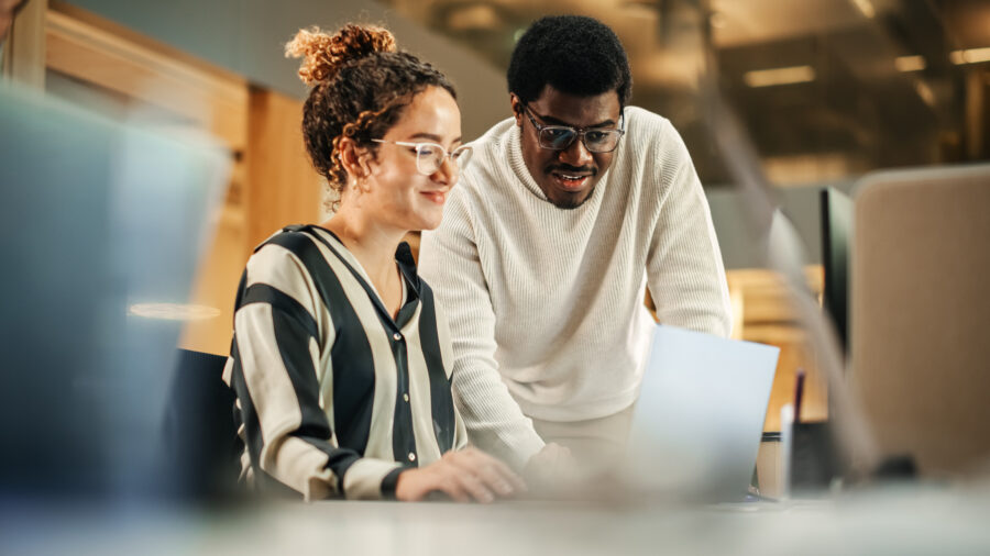 Two coworkers look at a laptop in an office together.