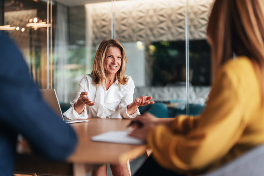 A business woman speaks to two people during a meeting in a modern office.