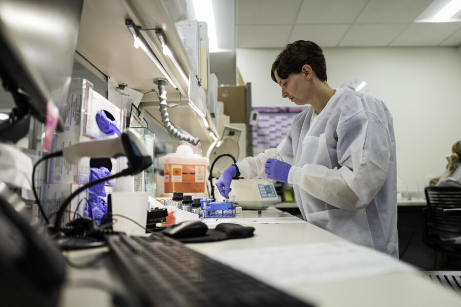 A lab worker in protective gear organizes test tubes.