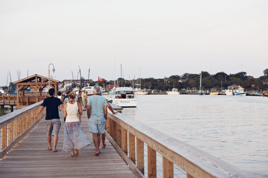 Three people walk down a boardwalk during the summer.