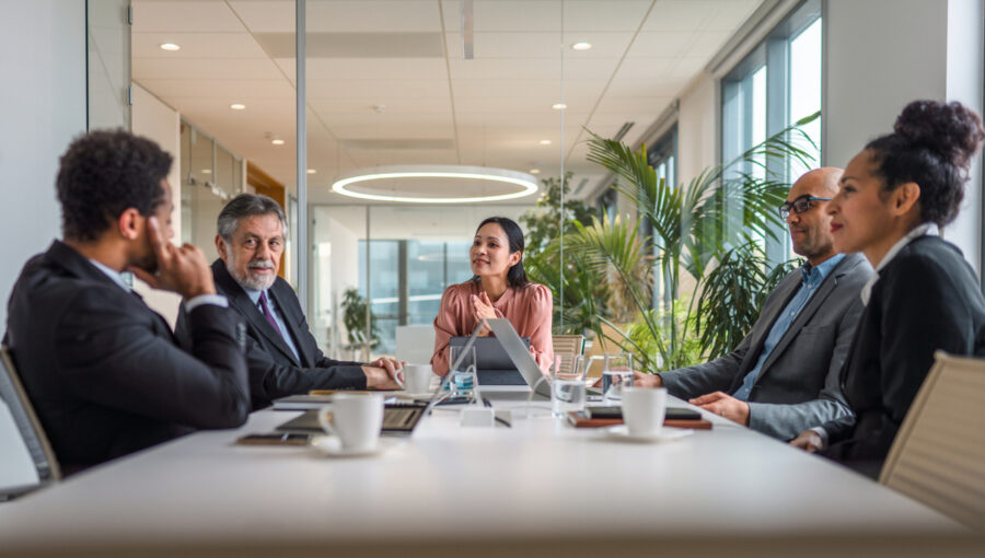 A group of business people sit around a boardroom table in a modern office.