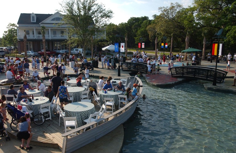 Groups of people sit at tables by the water during the day.