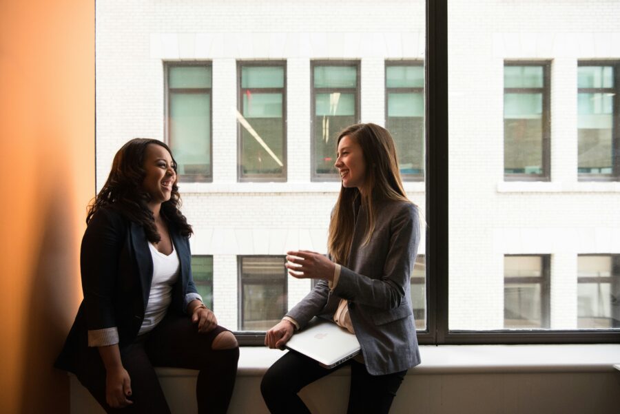 Two business women chat by a window in their office.
