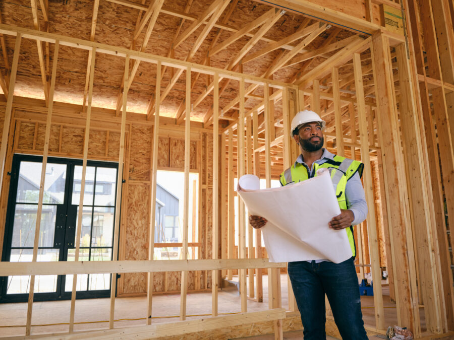 A construction worker in protective gear looks at blueprints in a building under construction.