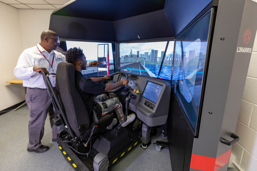 A student uses a truck driving simulator with an instructor supervising.