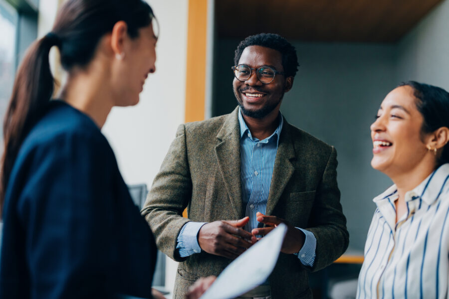 A group of three coworkers smile as they converse.