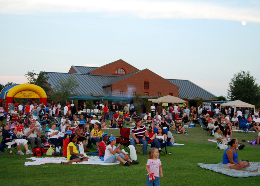 A crowd of people picnics on the grass during a festival.