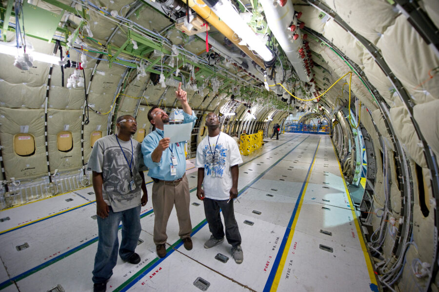 An aviation worker guides two students through the interior of an aircraft in construction.