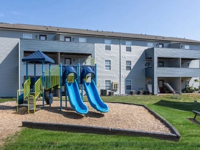 A children's playground behind an apartment complex during the day.