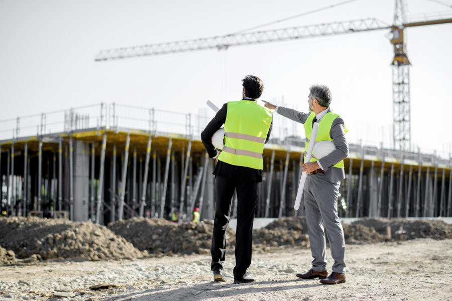 Two business men in hazard vests look out at a construction site during the day.