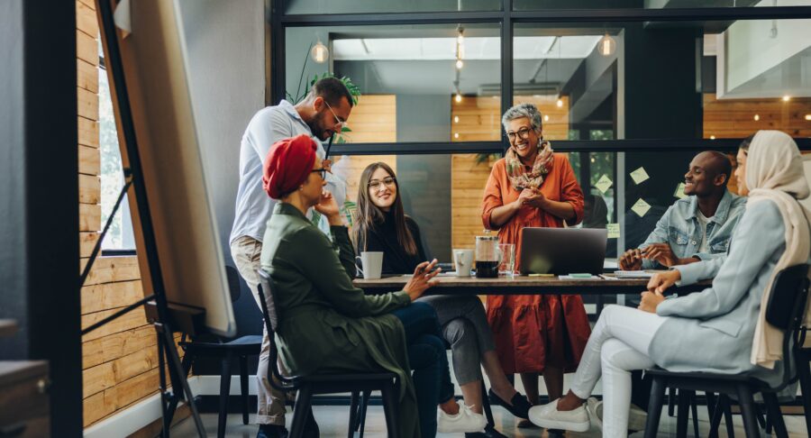 A group of diverse coworkers chat around a table in a modern office.