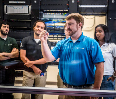 A Boeing employee writes on a board while his coworkers look on.