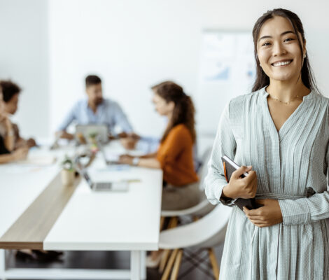A young woman in a modern office smiles at the camera.